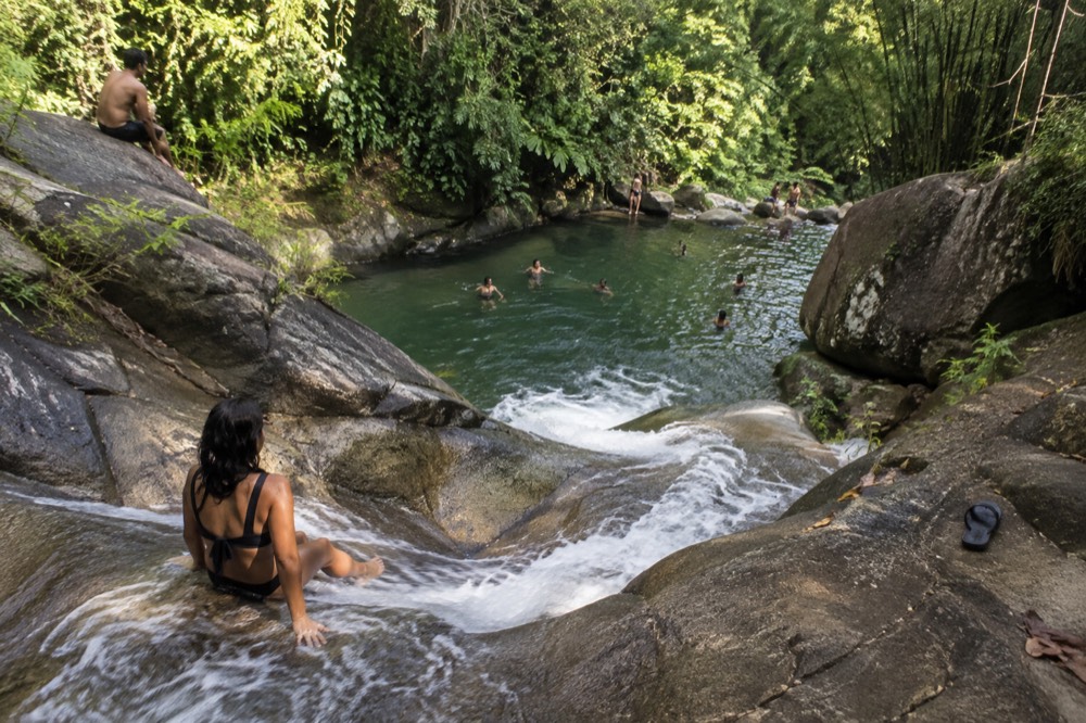 A natural rock waterslide with water flowing into a clear jungle pool