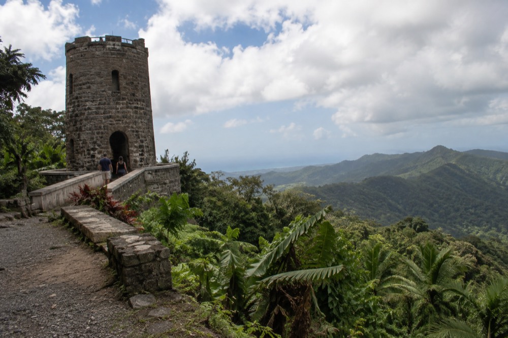 Stone observation tower overlooking layered green mountains under scattered clouds