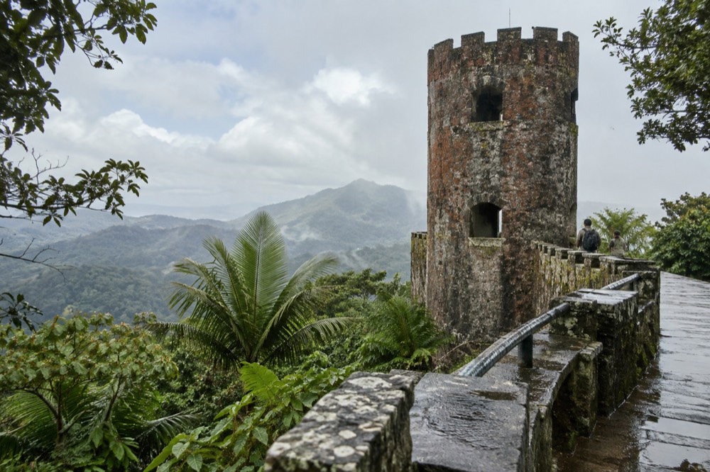 A stone observation tower above a green rainforest canopy with mist on distant ridges