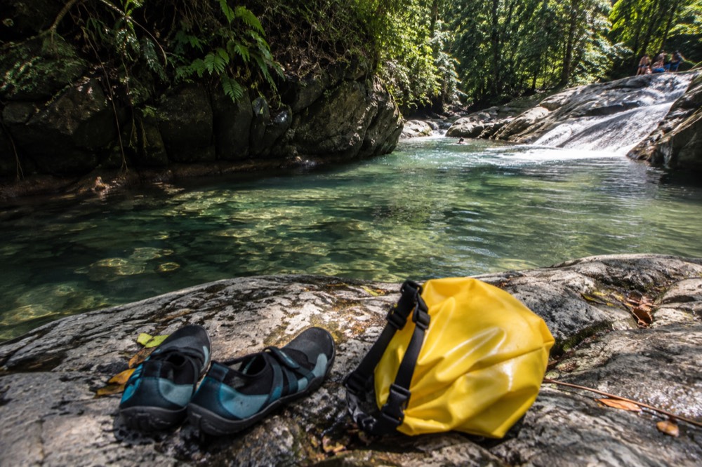 Water shoes and a dry bag resting on a rock beside a clear river pool
