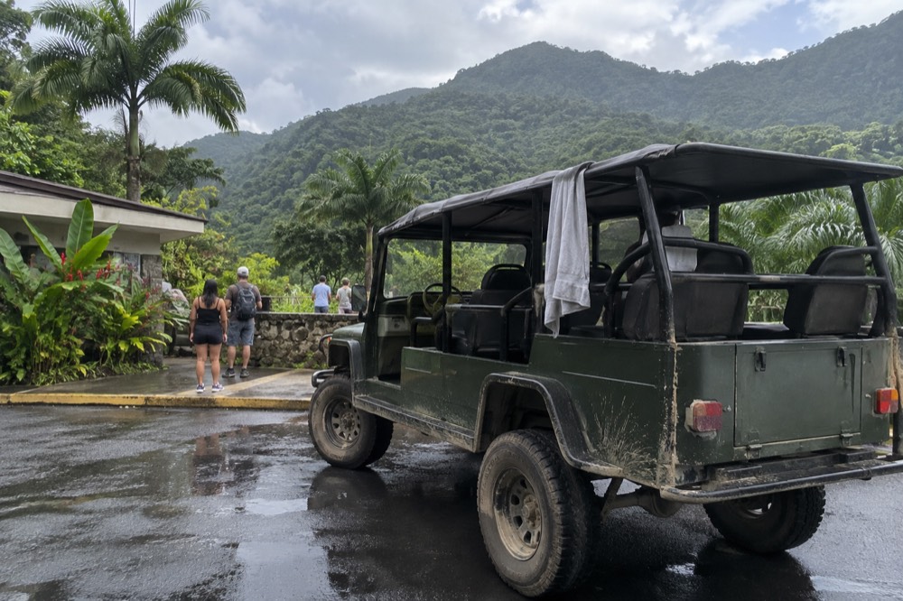 An open-topped tour vehicle parked on a wet mountain road beside tall green forest