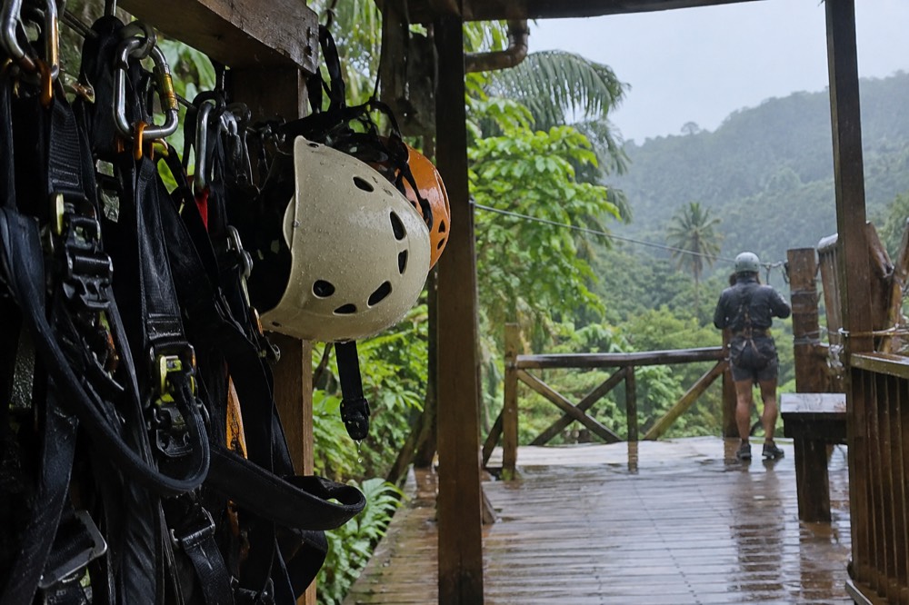 Harnesses and helmets arranged on a rack beside a zipline platform in the rainforest