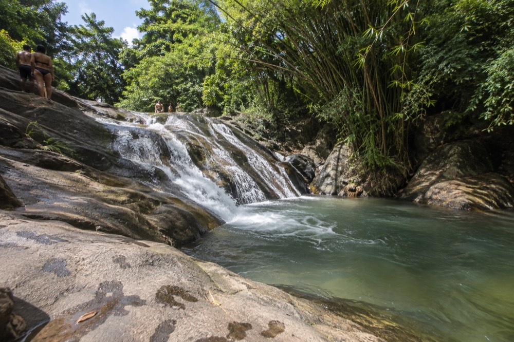 A natural rock waterslide with clear water flowing into a jungle pool