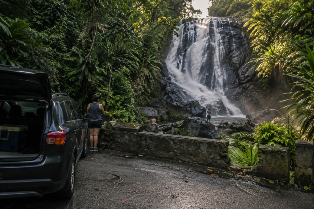 A wide waterfall spilling over a tall rock face into a boulder-lined pool