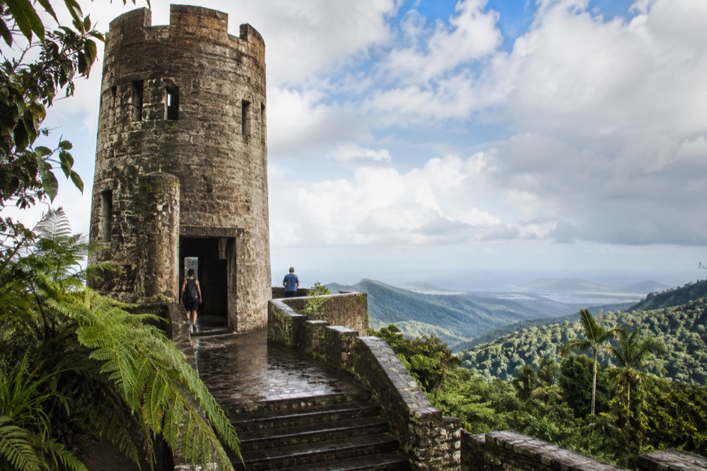 A stone observation tower rising above layered green rainforest ridges fading into coastal haze
