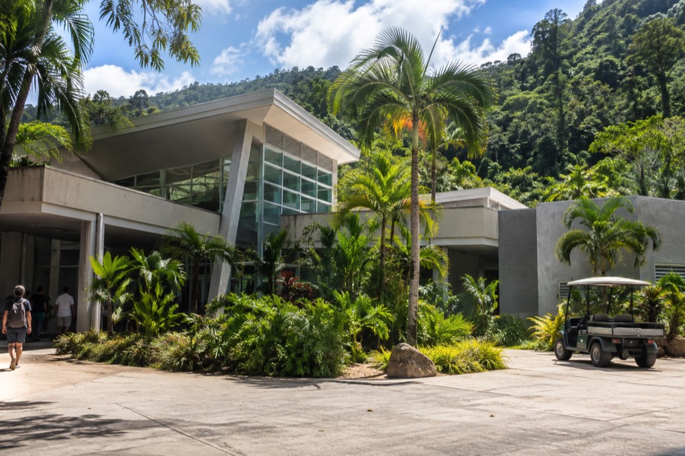 Modern visitor center building with tropical landscaping and forested hillside behind